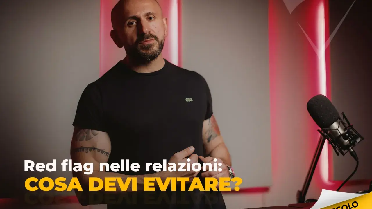 Uomo con tatuaggi parla di "red flag esempi" nelle relazioni. Microfono e luci rosse creano atmosfera da podcast.
