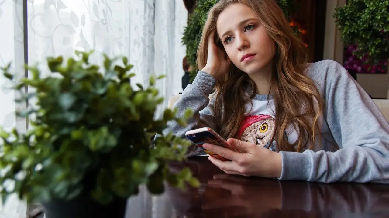 Ragazza pensierosa al telefono, con un'espressione che sembra dire "lei mi scrive e poi sparisce".