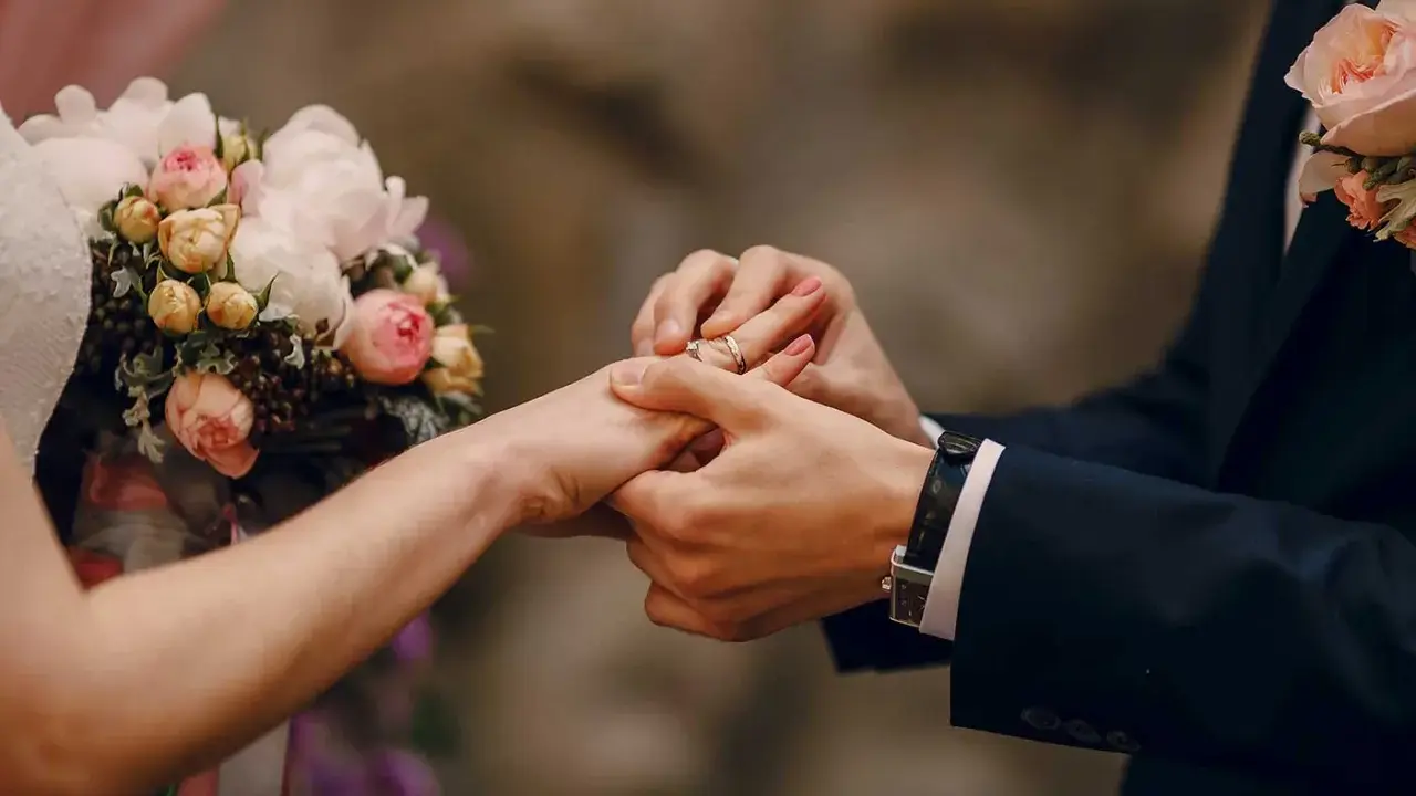 Scambio di fedi nuziali, un momento magico che ricorda un'agenzia matrimoniale gratis. Un bouquet di rose rosa e bianche completa la scena.