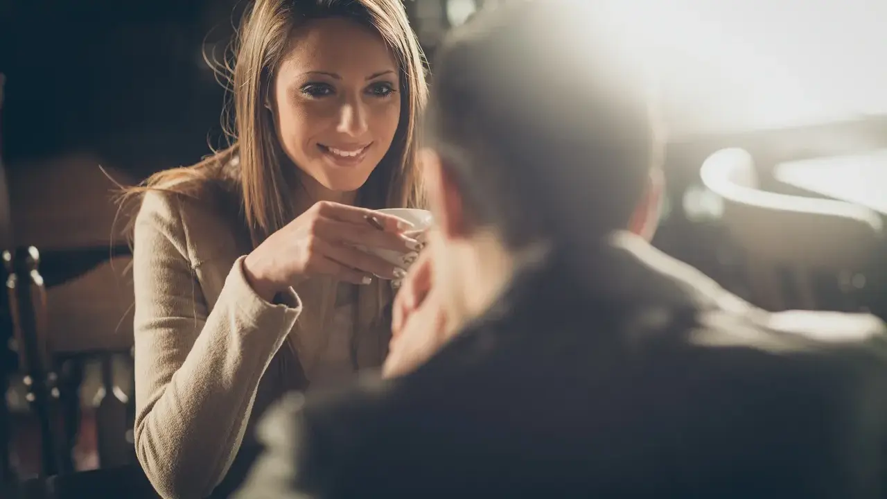 Lei sorride mentre beve un caffè, pensando a come chiedere di uscire per messaggio.