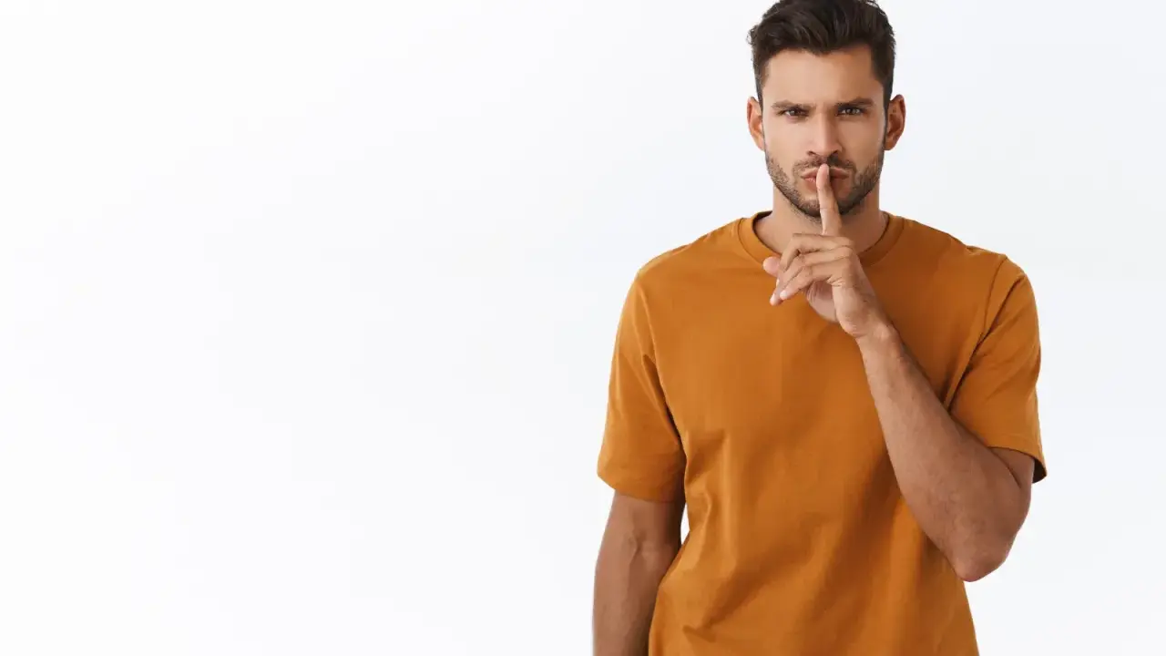 Uomo con dito sulle labbra, sguardo intenso. Sembra dire "shhh", forse perché un uomo non risponde ai messaggi.