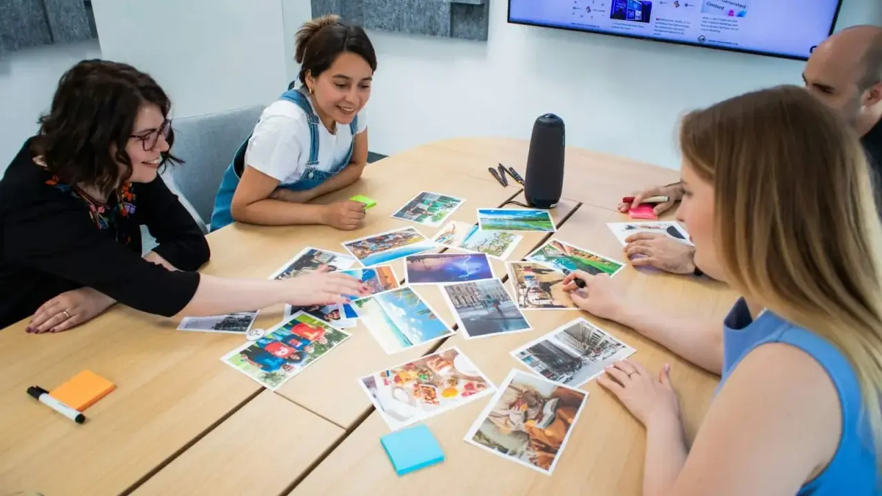 Persone attorno a un tavolo discutono immagini, trovando spunti di conversazione per un progetto creativo.