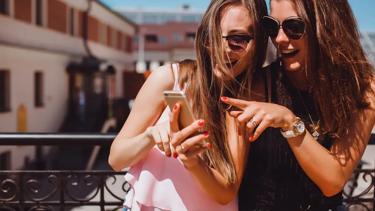 Due amiche ridono guardando il telefono, un momento perfetto per decidere cosa raccontare ad una ragazza.