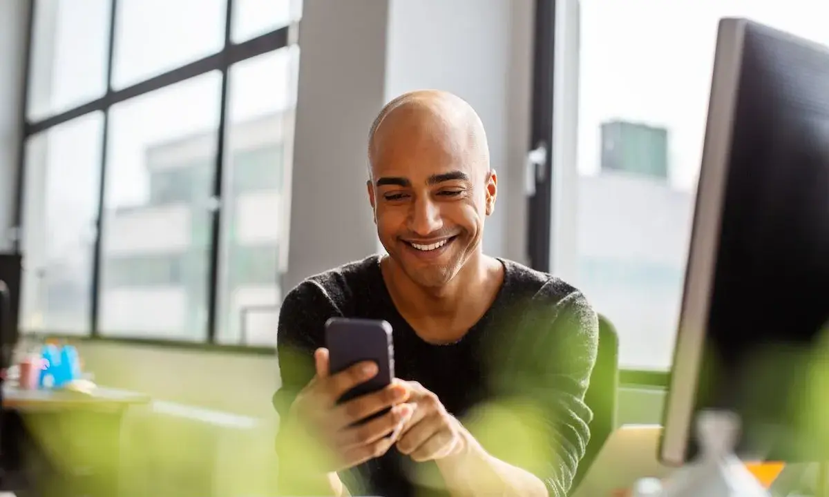 Uomo sorridente guarda il telefono, forse cercando frasi per approcciare qualcuno.