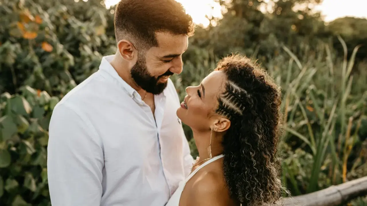 Un uomo e una donna si guardano con uno sguardo innamorato, circondati da una vegetazione lussureggiante al tramonto.