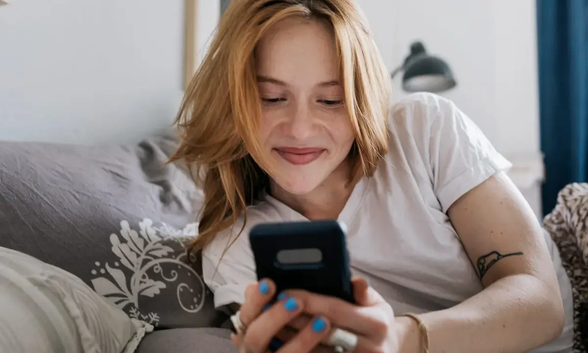 Ragazza con capelli rossi sorride guardando il telefono. Mi scrive ma non mi chiede di uscire, sperando in un invito.