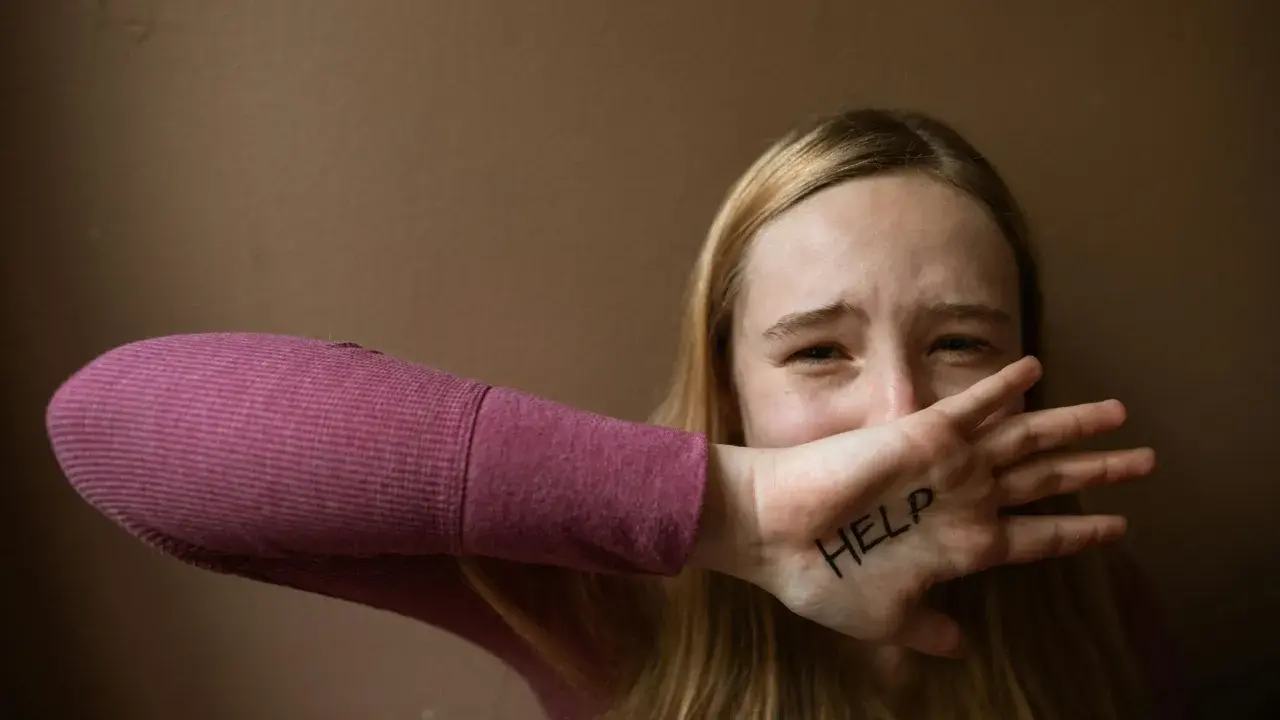 Ragazza con "HELP" scritto sulla mano, copre la bocca con espressione disperata. Un chiaro segnale di red flag relazione.
