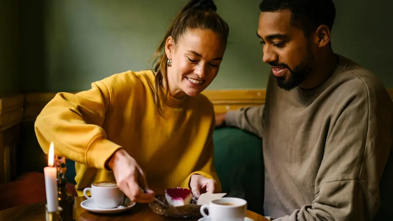 Coppia sorridente condivide un dolce, tra caffè e candela. Un momento intimo perfetto per porre domande da fare per conoscersi.