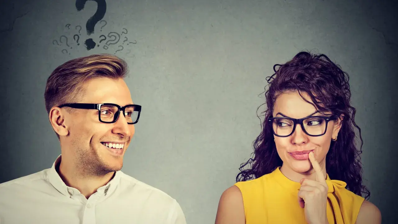 Uomo sorridente guarda donna pensierosa, con punti interrogativi sopra la testa. Come capire se gli piaci ma lo nasconde?