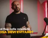 Uomo con tatuaggi parla di "red flag esempi" nelle relazioni. Microfono e luci rosse creano atmosfera da podcast.