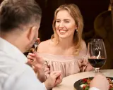 Coppia a cena, lei sorride mentre lui mangia. Forse stanno parlando di dove trovare sugar daddy per una vita di lusso.