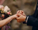 Scambio di fedi nuziali, un momento magico che ricorda un'agenzia matrimoniale gratis. Un bouquet di rose rosa e bianche completa la scena.