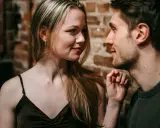 Un uomo e una donna si guardano intensamente. Lei ha lo sguardo di chi ti vuole, un sorriso accennato e i capelli biondi sciolti. Lui è vicino, con un'espressione concentrata.