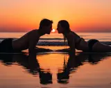 Coppia sdraiata sulla spiaggia al tramonto, sguardi intensi, si sente l'attrazione tra due persone.