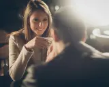 Lei sorride mentre beve un caffè, pensando a come chiedere di uscire per messaggio.