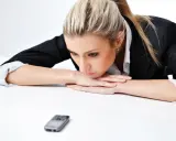 Donna bionda con giacca nera appoggiata sul tavolo, telefono in primo piano. Riflette su cosa scrivere ad un uomo che non ti cerca.