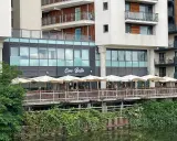 Ristorante "Ciao Bella" con tavoli all'aperto sotto ombrelloni bianchi, affacciato su un canale. Un complimento che invita a gustare la cucina italiana.