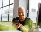 Uomo sorridente guarda il telefono, forse cercando frasi per approcciare qualcuno.