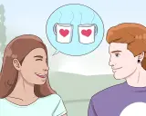 Una ragazza sorride mentre pensa a come iniziare una conversazione con un ragazzo, immaginando due tazze con cuori.