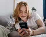 Ragazza con capelli rossi sorride guardando il telefono. Mi scrive ma non mi chiede di uscire, sperando in un invito.