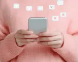 Mani con smartphone, icone di like e play fluttuano, evocando la psicologia di chi fa orbiting e cerca conferme digitali.