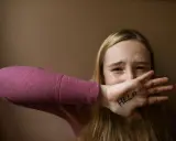 Ragazza con "HELP" scritto sulla mano, copre la bocca con espressione disperata. Un chiaro segnale di red flag relazione.