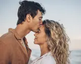 Un uomo bacia la fronte di una donna sulla spiaggia. Se una persona non ti cerca, forse è perché ha già trovato ciò che cercava.