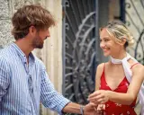 Un uomo con una camicia a righe fa l'occhiolino e sorride a una donna con un vestito rosso. Un momento di complicità.