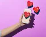 Mano con smartphone che mostra un cuore rosso, circondata da palloncini a forma di cuore. Simboleggia i comportamenti di un uomo non interessato, che ignora i segnali d'affetto.