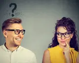 Uomo sorridente guarda donna pensierosa, con punti interrogativi sopra la testa. Come capire se gli piaci ma lo nasconde?