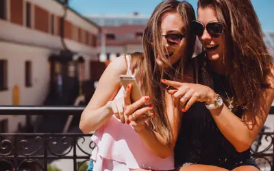 Due amiche ridono guardando il telefono, un momento perfetto per decidere cosa raccontare ad una ragazza.