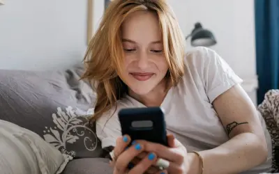 Ragazza con capelli rossi sorride guardando il telefono. Mi scrive ma non mi chiede di uscire, sperando in un invito.