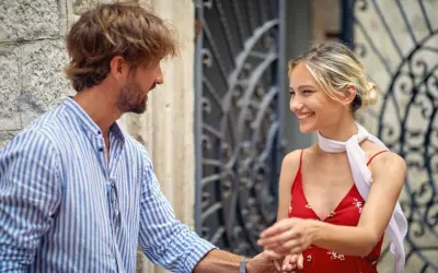 Un uomo con una camicia a righe fa l'occhiolino e sorride a una donna con un vestito rosso. Un momento di complicità.