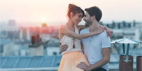 Coppia sul tetto al tramonto, sguardi complici e abbracci che rivelano segnali nascosti di attrazione.