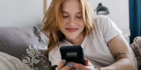Ragazza con capelli rossi sorride guardando il telefono. Mi scrive ma non mi chiede di uscire, sperando in un invito.