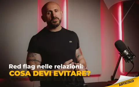 Uomo con tatuaggi parla di "red flag esempi" nelle relazioni. Microfono e luci rosse creano atmosfera da podcast.