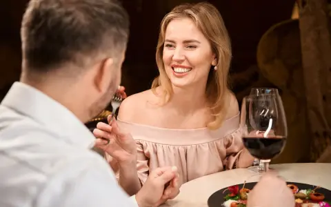 Coppia a cena, lei sorride mentre lui mangia. Forse stanno parlando di dove trovare sugar daddy per una vita di lusso.