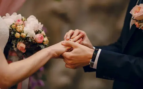 Scambio di fedi nuziali, un momento magico che ricorda un'agenzia matrimoniale gratis. Un bouquet di rose rosa e bianche completa la scena.