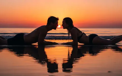 Coppia sdraiata sulla spiaggia al tramonto, sguardi intensi, si sente l'attrazione tra due persone.