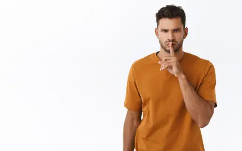 Uomo con dito sulle labbra, sguardo intenso. Sembra dire "shhh", forse perché un uomo non risponde ai messaggi.