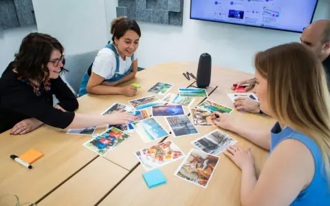 Persone attorno a un tavolo discutono immagini, trovando spunti di conversazione per un progetto creativo.