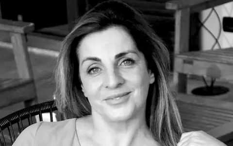 Ritratto in bianco e nero di una donna sorridente, con i capelli lunghi e mossi. "Ciao, come stai?" è una domanda inutile se il tuo sguardo è così sereno.