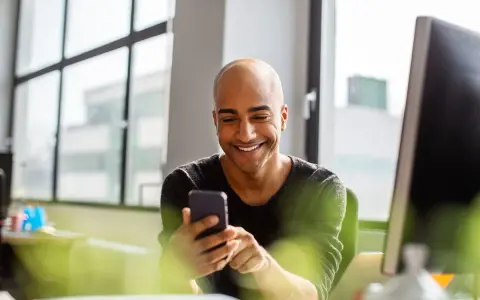 Uomo sorridente guarda il telefono, forse cercando frasi per approcciare qualcuno.