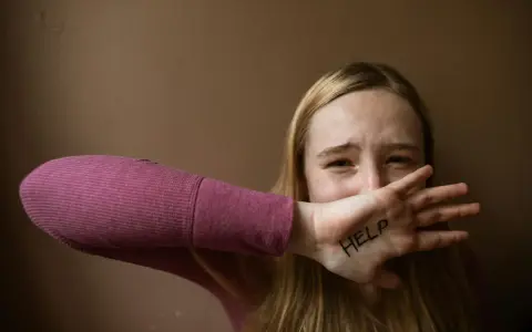 Ragazza con "HELP" scritto sulla mano, copre la bocca con espressione disperata. Un chiaro segnale di red flag relazione.