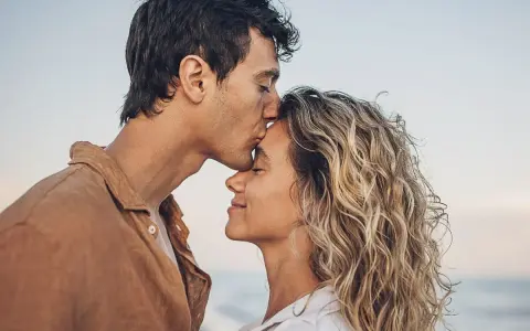 Un uomo bacia la fronte di una donna sulla spiaggia. Se una persona non ti cerca, forse è perché ha già trovato ciò che cercava.