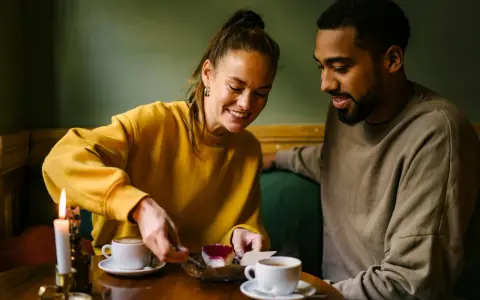 Coppia sorridente condivide un dolce, tra caffè e candela. Un momento intimo perfetto per porre domande da fare per conoscersi.