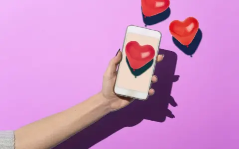 Mano con smartphone che mostra un cuore rosso, circondata da palloncini a forma di cuore. Simboleggia i comportamenti di un uomo non interessato, che ignora i segnali d'affetto.
