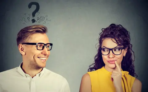 Uomo sorridente guarda donna pensierosa, con punti interrogativi sopra la testa. Come capire se gli piaci ma lo nasconde?