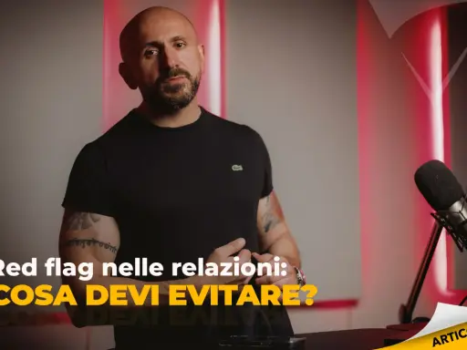 Uomo con tatuaggi parla di "red flag esempi" nelle relazioni. Microfono e luci rosse creano atmosfera da podcast.