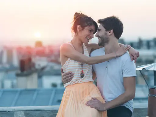 Coppia sul tetto al tramonto, sguardi complici e abbracci che rivelano segnali nascosti di attrazione.